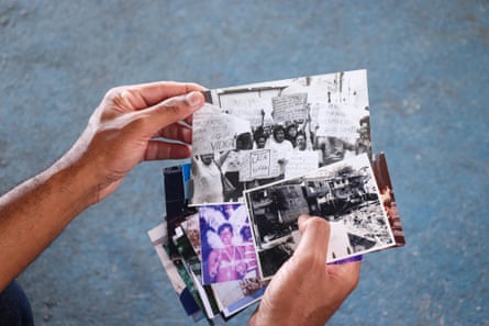 Two hands holding a collection of photos, one being a monochrome pic of protesters holding placards and another of a woman in Carnival costume with feather headdress