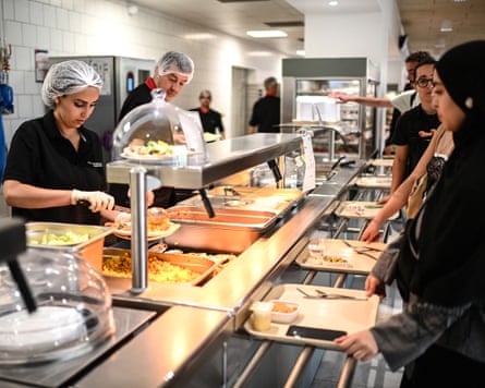 Employees serve dishes to students queueing up prior to a meal at a university restaurant