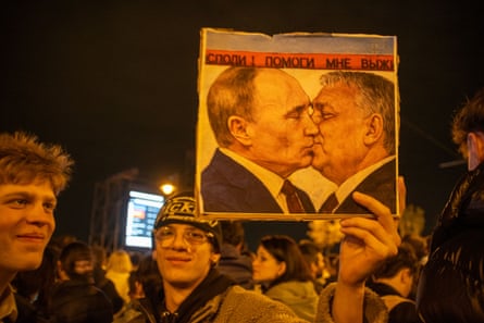 A supporter of the Tisza party holds up a poster showing Vladimir Putin and Viktor Orbán kissing on the lips
