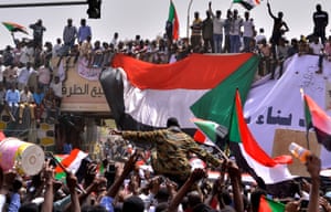 A military officer is carried by the crowd as demonstrators wave flags