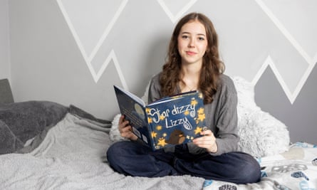 Avalyn Godfrey sitting on a bed, holding the book that she wrote and illustrated, Star Dizzy Lizzy.