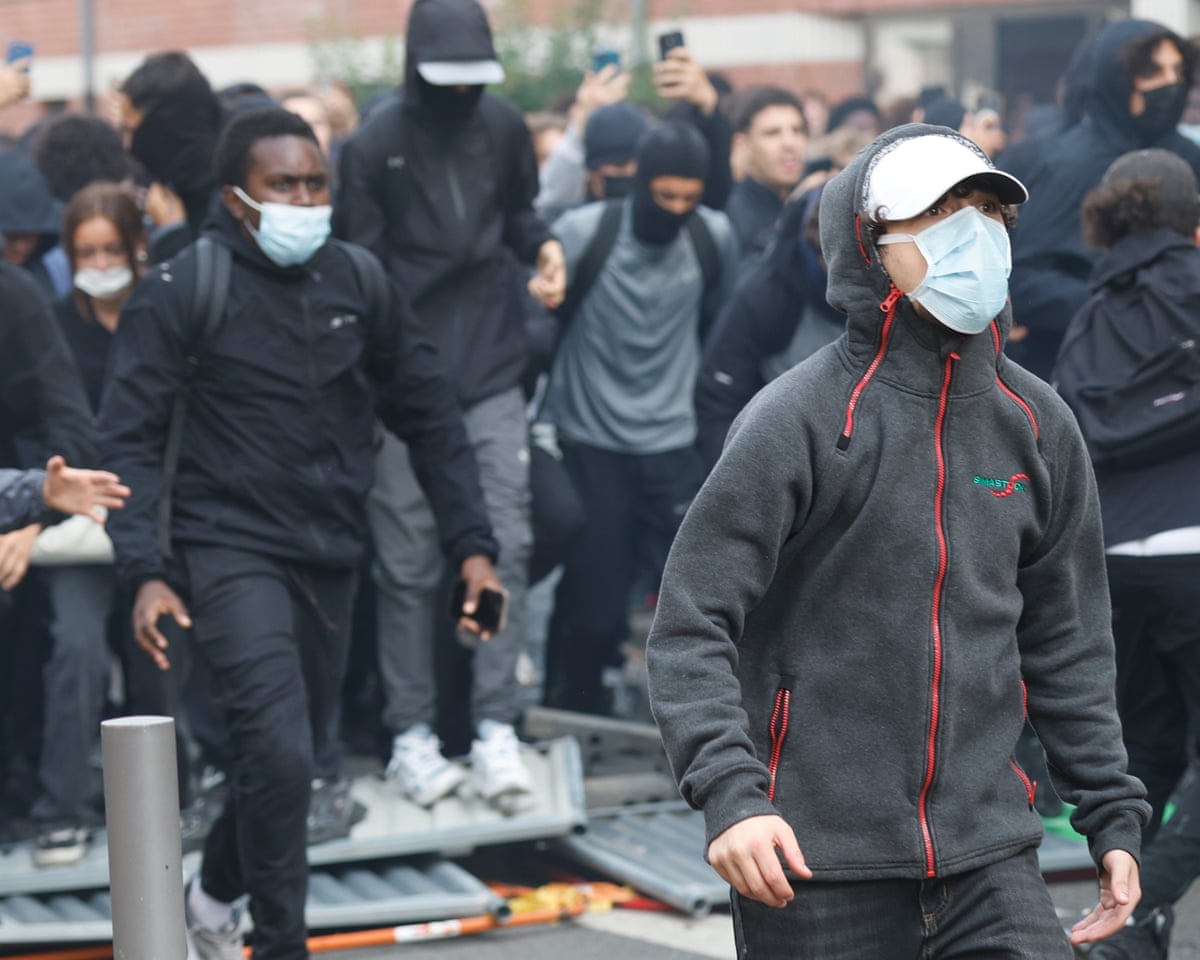 Crowd of young people, mainly male, wearing black and many with masks