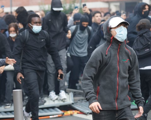 Crowd of young people, mainly male, wearing black and many with masks