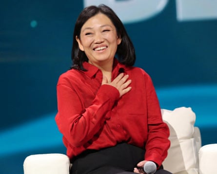 Tatyana Kim, wearing a red shirt and black trousers, sits on a low chair holding a microphone