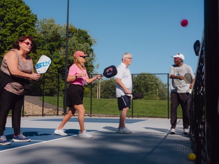 A man holding a square paddle gives instruction to three older adults holding similar paddles on a court.