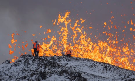 Scientist take measurements and samples standing on a ridge in front of the eruptive fissure of the volcano in Grindavik.