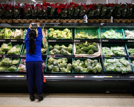 A worker adjusts a price sign in a supermarket vegetable aisle