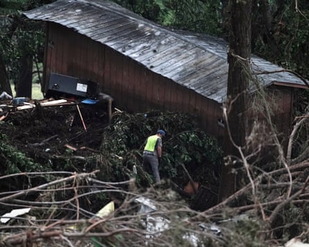 worker in neon vest stands in pile of debris from flood next to a damaged building
