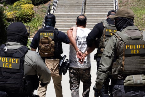 Masked men in tactical gear lead a handcuffed man to a staircase