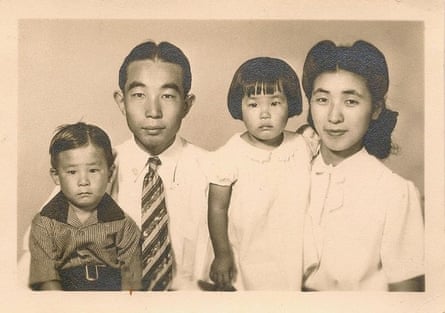 Black-and-white/sepia tone image of mom, dad, and two young kids sitting together. Parents are smiling slightly; kids are not.