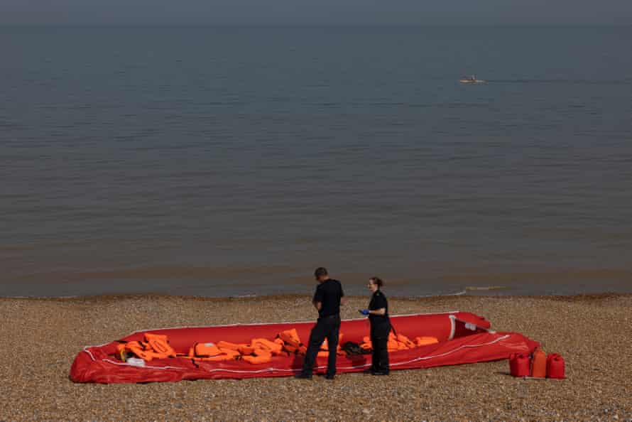 Border force officials inspect an inflatable dinghy, discarded on a beach after being used by migrants to cross the English Channel, in Walmer
