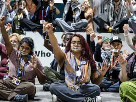 Activists sit on the floor with tape over their mouths that reads ‘Pay up!’