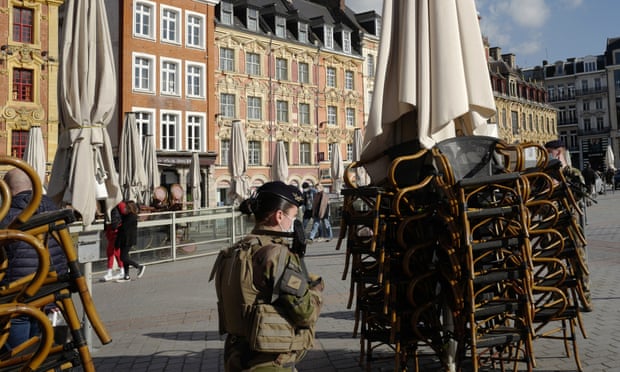 A soldier walks past stacked chairs in front of a cafe in Lille, northern France