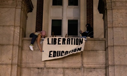 Two protesters hang a sign from a balcony reading: ‘Liberation, education.’
