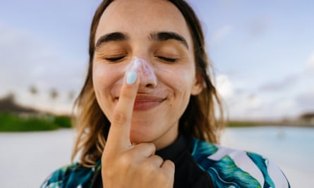 A young woman applies sunscreen to her nose