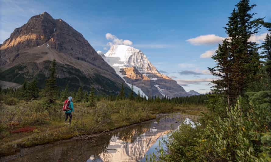 A hiker on the Berg Lake trail with Mt. Robson’s reflection and Rearguard mountain in the foreground, Mt. Robson Provincial Park, British Columbia.