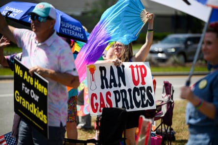 A woman holds a sign that reads ‘I Ran Up Gas Prices’ with a figure of Trump
