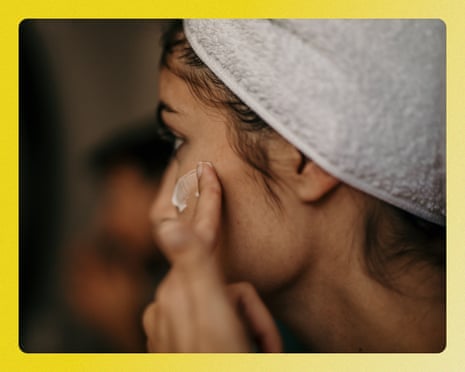 Image 2: A smiling mixed race young woman applying moisturizer on her face in the bathroom