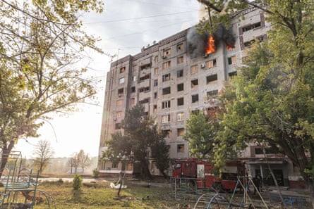 Firefighters attempt to put out a fire in a residential building. Flames and smoke and billowing from windows on an upper floor of a large concrete block.