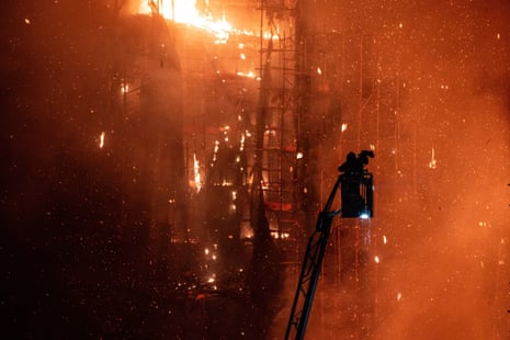 A firefighter on a fire truck ladder as smoke and flames rise at Wang Fuk Court