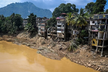 Flood-damaged buildings at the side of a river with a mountain in the background