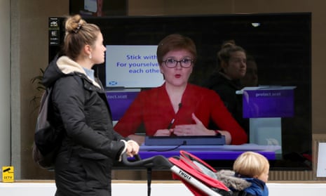 A woman with a pushchair walks past an image of Nicola Sturgeon on a TV screen