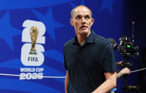 Thomas Tuchel standing at a press conference with a FIFA World Cup 2026 and a TV camera behind him