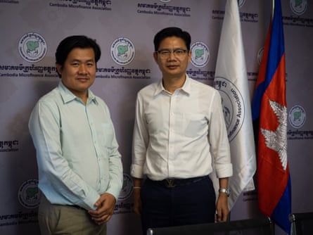 Two businessmen in shirts standing in front of a wall hung with a Cambodian flag and a flag for the Cambodia Microfinance Association