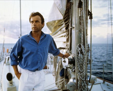 Sam Neill successful a ray bluish linen garment and achromatic trousers adjacent to nan mast of a yacht successful nan movie Dead Calm (1989).