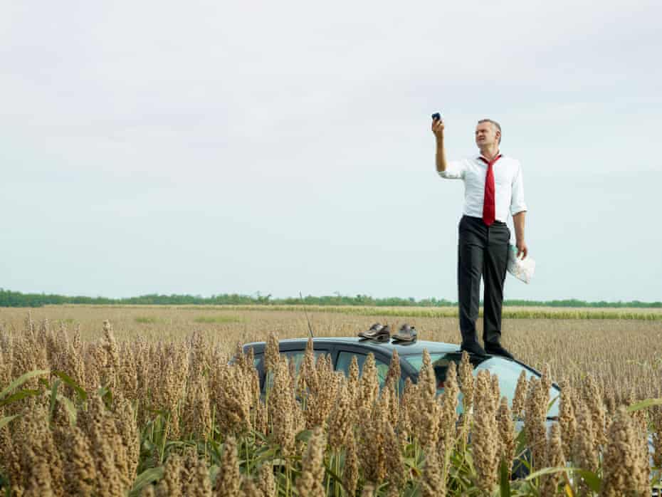 Man on top of his car in a field looking at his GPS