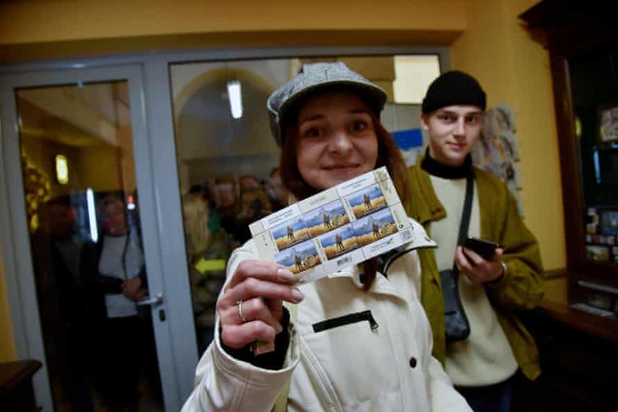 A woman in a post office in Lviv displays postage stamps featuring a Ukrainian soldier making a gesture at a Russian ship