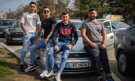 Four young men pose around a parked car