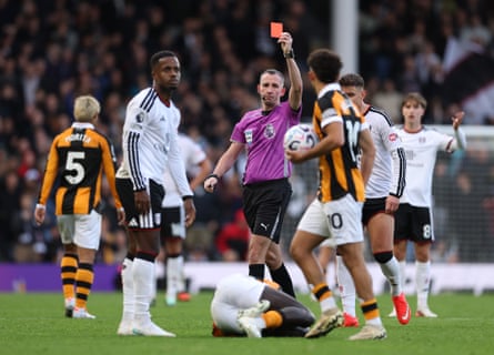Referee Chris Kavanagh holds up a red card as players look on, with one lying on the pitch