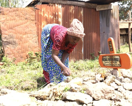 Margaret Njeri Murigi stoops over a grave covered in rocks