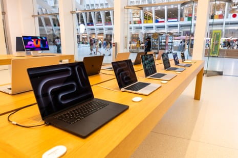 Multiple laptops are displayed open on a long wooden table in an Apple store