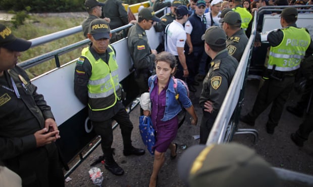 Police stand guard as a Venezuelan woman crosses into Colombia through a bridge linking San Antonio del Tachira, Venezuela, with Cucuta, Colombia.