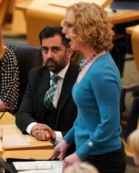 Humza Yousaf sits at a table watching Lorna Slater speaking on her feet