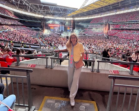 Amy Frye stands in the crowd at Wembley Stadium wearing cream trousers, a yellow polo shirt and a tie she customised with the word POP.