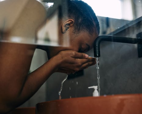A woman washing face with water in bathroom sink