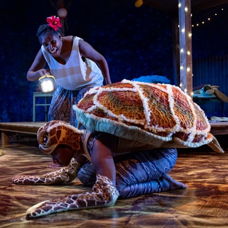 Kaplumbağa kabuğu ve palet takan dansçı yere eğilirken başka bir sanatçı üzerlerine meşale tutuşturuyor