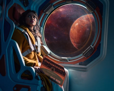 Belinda sits next to a porthole on a spaceship, through which an alien world can be seen.