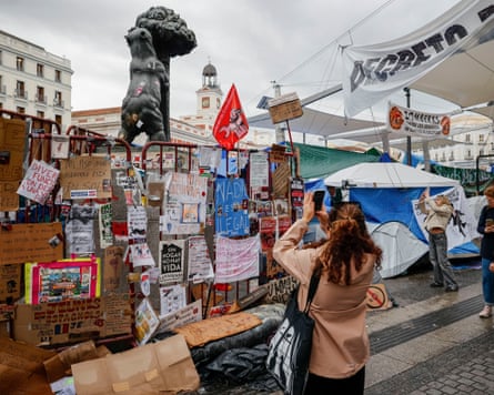 People take photos of a statue of bear and a tree surrounded by tents and placards