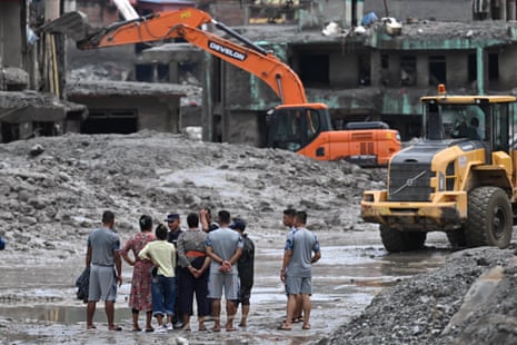 Residents watch as an excavator helps people to collect some of their belongings from their house in the aftermath of flash floods