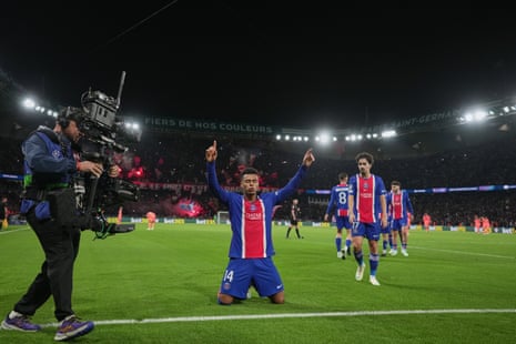 Desire Doue kneels with arms raised, celebrating a goal as teammates approach