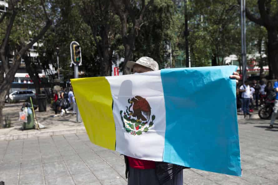 A man holds up a Mexican flag during a protest. The traditional red, white and green colors of the flag have been replaced with yellow, white and blue to honor Ukraine.