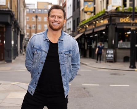 Joe Swash standing on a city street in front of a pub