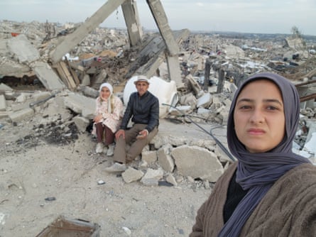 Malak Tantesh and her father, Amjed, sit among the rubble of their home as Malak’s sister, Enas, takes a picture