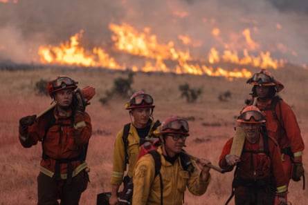 Five men and women in heavy orange and yellow fire gear with fire behind them.