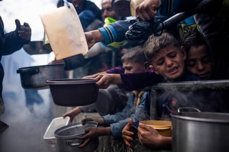 Children crowd and hold out empty dishes as they wait for food.
