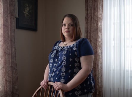 A woman in a blue top standing up holding the back of a chair